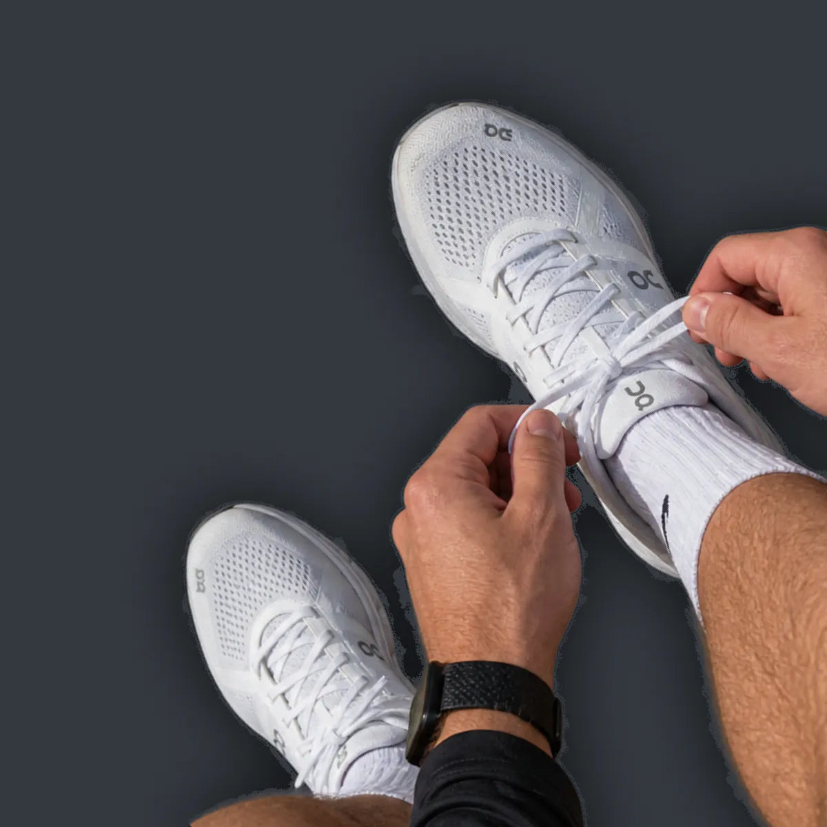 A POV image of a man tying the laces on white running shoes, worn with white socks.