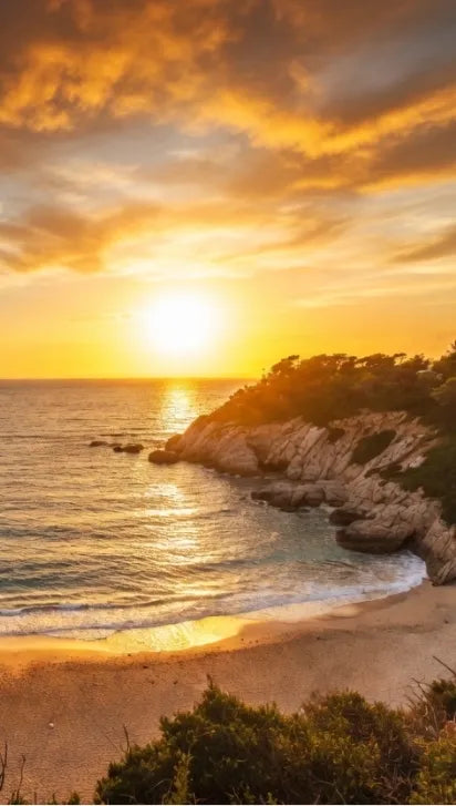 A scenic coastal cove on the Costa Brava at sunset with golden clouds, turquoise water, sandy beach, rocky cliffs, and green vegetation in the foreground.